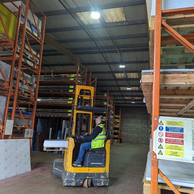 Durable lighting is important for demanding conditions like busy warehouses. Picture of man on forklift truck in a warehouse